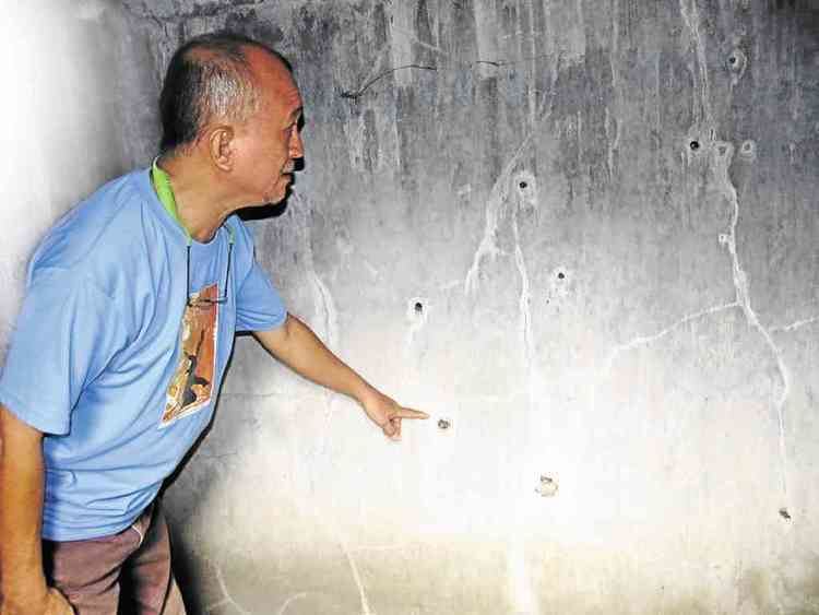 Bernie Salcedo is pointing the bullet holes on the wall where Evelio B. Javier was assassinated. Bernie is wearing a blue shirt and brown shorts.