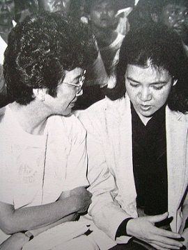 President Cory Aquino and Precious Javier are talking in the wake of Evelio Javier in February 1986. President Cory wearing eyeglasses and a white dress while Precious wearing a white blazer over a black long sleeve top.