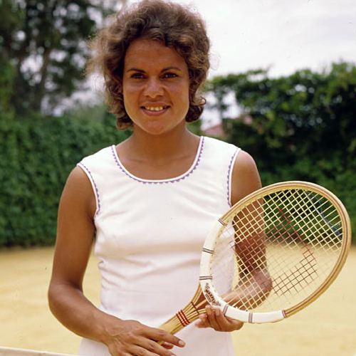 Evonne Goolagong Cawley smiling and holding racket while wearing white dress