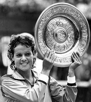 Evonne Goolagong Cawley smiling while holding her Wimbledon trophy