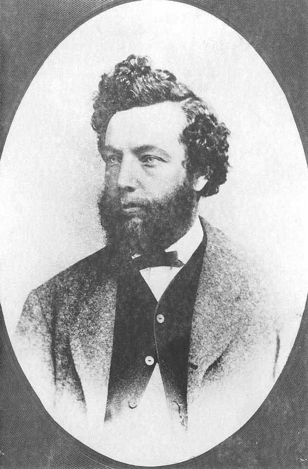 Charles Roscoe Savage with curly hair, mustache, beard and wearing a suit and a bow tie.