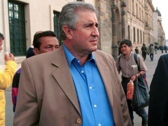 Fabio Ochoa Vásquez looking serious while walking on a street and wearing a blue shirt under a brown coat