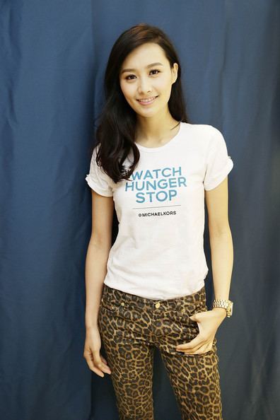 Fala Chen smiling at the Michael Kors World Food Day while wearing a white shirt, animal print pants, and wristwatch