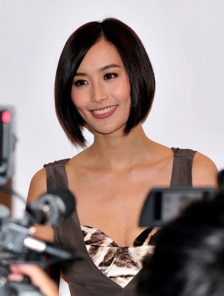 Fala Chen smiling while people taking pictures of her and ​wearing a brown and white sleeveless dress