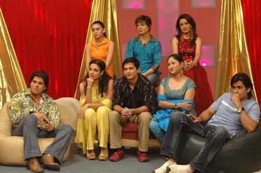 In the movie scene of Fame Gurukul 2005, the celebrity judges in a room with a cream chair and black chair,, behind is red and gold curtains. At the back, from left, Shreya Ghoshal is serious, sitting, hands on lap, has black hair, wearing a orange collar sleeveless dress, 2nd from left, Alisha Chinoy is Serious, Sitting,The ankle of left leg rests right above the knee of the right leg, has short brown hair, wearing a blue with collar long sleeve and a denim pants, 3rd from left, Bipasha Basu is serious, sitting, legs crossed both hands together at her knees, has long black hair, wearing a long earrings and a red dress,  in front of them, from left, John Abraham is serious, sitting hands over his lap, has black hair, wearing a cream with olive green print long sleeve, a gray pants and brown leather shoes,  2nd from left, Bhumika Chawla is serious, sitting, right hand under her chin and elbow leaning on top of her leg, left hand resting on her lap, has black curly hair, wearing earrings, yellow top with yellow scarf, yellow pants, and yellow shoes, 3rd from left, Karan Johar is serious, sitting, arms over his lap hands together, has black hair, wearing a black with white stripes long sleeve, khaki pants, and brown shoes. 4th from left, Alka Yagnik is serious, sitting arms crossed, wearing earrings, a gray top, a light blue scarf and blue pants, On the right, Aftab Shivdasani is serious, Sitting on a black chair, leaning backwards, left arm bend hands closed on front of his mouth, right hand open on his right leg, wearing a wristwatch, a gray with white line shirt, gray denim pants, and cream shoes.