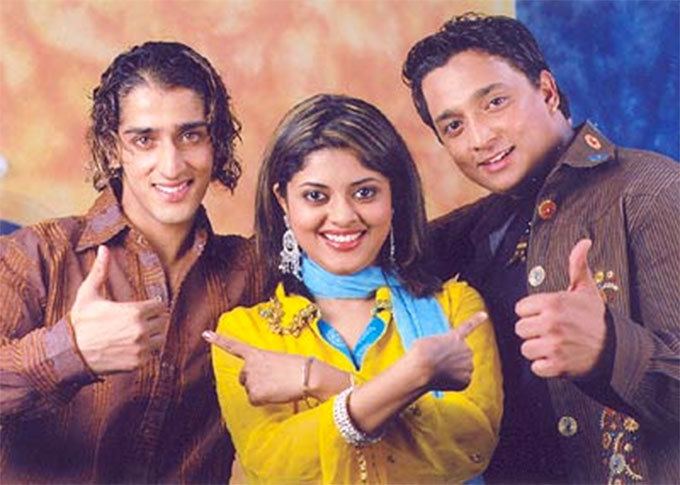 The top three contestants in Gurukul's Fame 2005 On the left, Qazi Touqeer is smiling, right-hand thumbs up has wavy hair with yellow highlights, and is wearing a brown-striped long-sleeve polo. In the middle is Ruprekha Banerjee, smiling, pointing her left finger to the right and right finger to the left, she has long black hair with yellow highlights and wears a large earring, a blue scarf, gold and silver bracelets, and a yellow long sleeve. On the right, Rex D'Souza is smiling, with his left-hand thumbs up, wearing a dark blue shirt and a brown jacket with large assorted buttons.