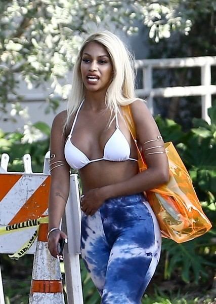 Fanny Neguesha while walking wearing a white bra and blue pants carrying an orange plastic bag