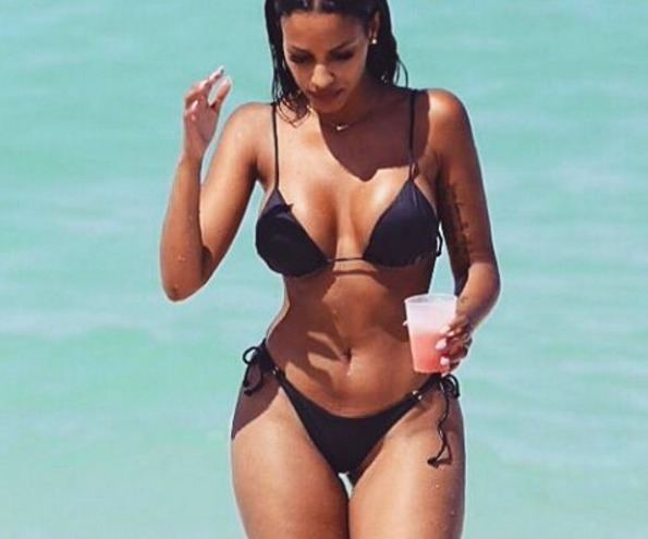 Fanny Neguesha in a beach wearing a black two-piece bikini while holding a plastic cup