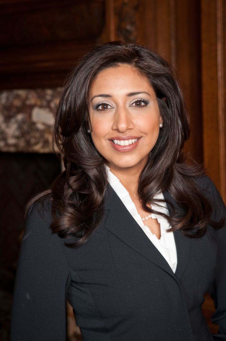 Farah Nasser smiling while wearing a black coat and white blouse