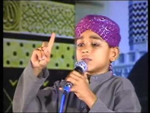 A younger Farhan Ali Qadri reciting on a stage and wearing a purple turban and a gray collared pakistani clothing.