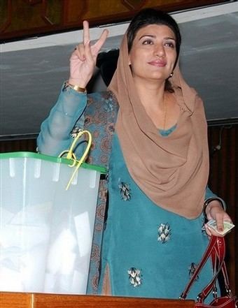Farzana Raja smiling, wearing a brown dupatta scarf, a blue traditional Indian clothing while doing a peace sign.