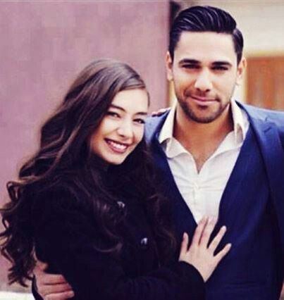 Neslihan Atagül smiling with Kadir Dogulu wearing a blue coat and white long sleeves