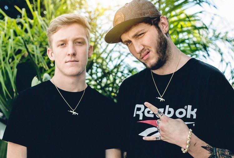 Tfue smiling with Faze Banks doing a wacky face with his finger pointing to Tfue and both wearing a black shirt and similar necklace