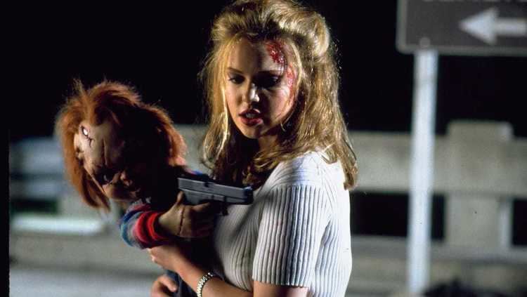 Katherine Heigl carrying the living doll named "Chucky" holding a gun and Katherine with a wound on the forehead while wearing a white blouse