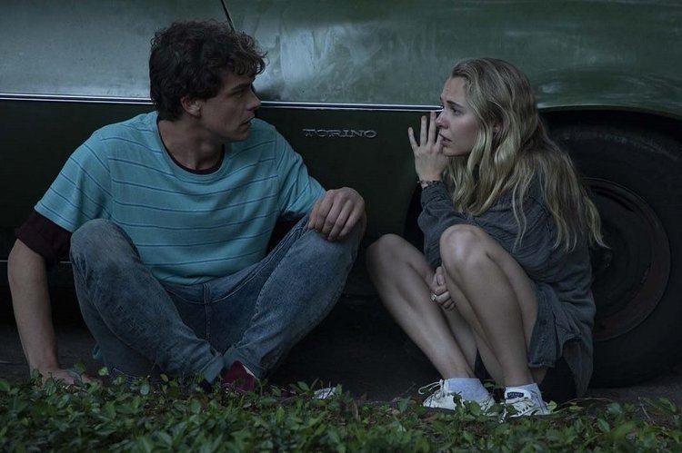 Israel Broussard looking terrified while hiding on the side of a car with Madison Iseman in a scene from the 2021 movie "Fear of Rain"
