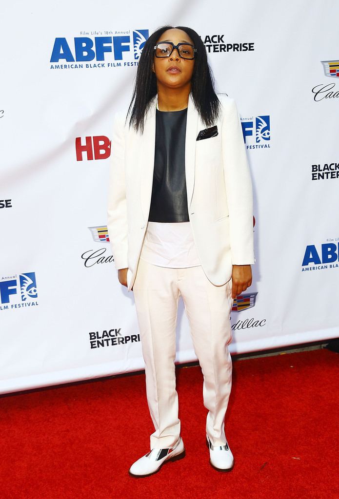 Felicia Pearson wearing eyeglasses, a white blazer, a black inner blouse, white pants, and white shoes