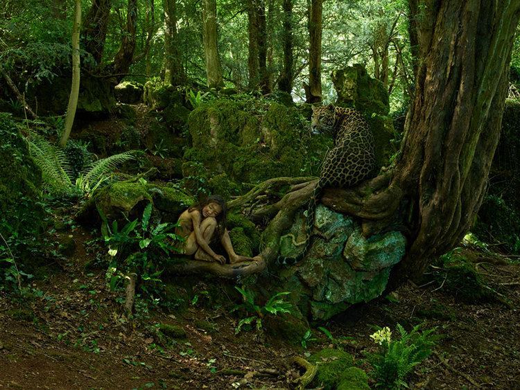 A young feral girl sitting on the root of a tree in the wild with a cheetah.