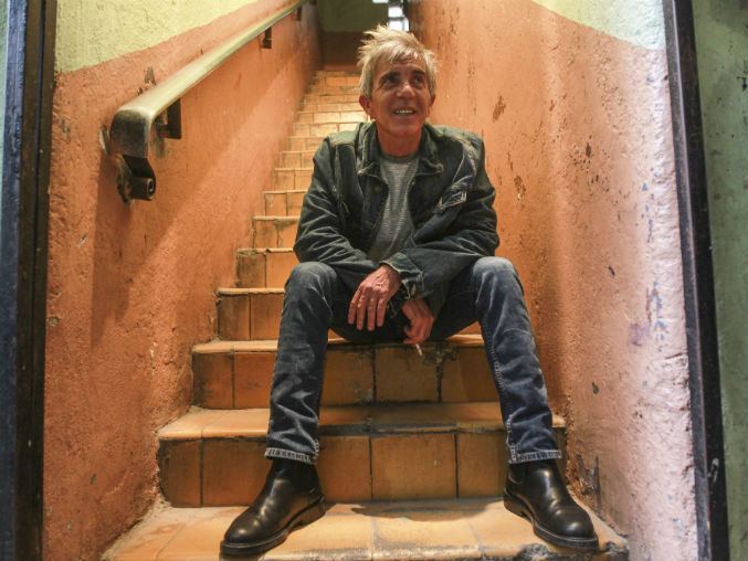 Fernando Ciangherotti smiling while sitting on the stairs and wearing a denim jacket, gray shirt, denim pants, and black shoes