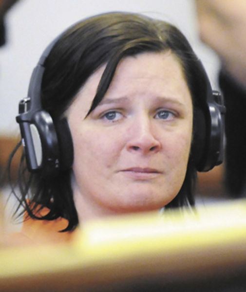 In a court appearance, Kathy Coy is sorrowful, has black hair, and a mole on her right cheek, wearing black headphones.