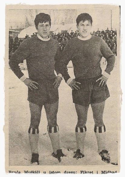Fikret with his teammate standing while hands are on their waist with serious faces and wearing long sleeve shirts, shorts, high socks, and shoes.