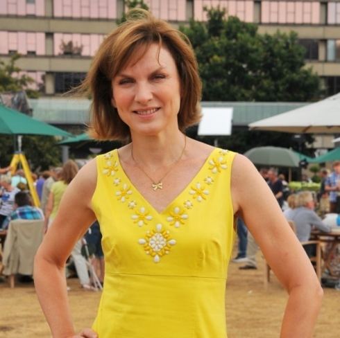 Fiona Bruce with blonde hair, a necklace, and a yellow sleeveless top.