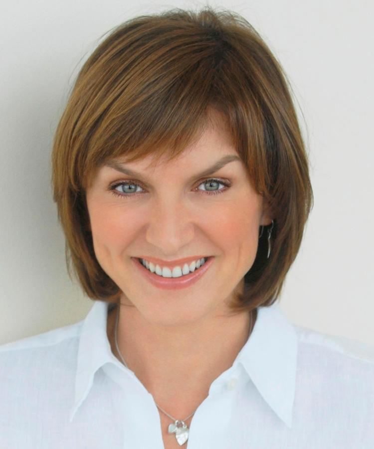 Fiona Bruce with blonde hair, wearing earrings, a necklace, and a white polo shirt.