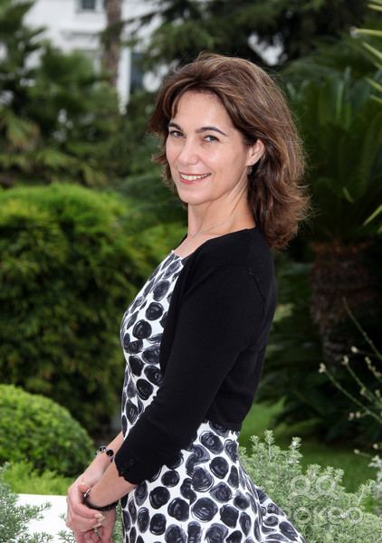 Fiona Dolman smiling, with short blonde hair, wearing a black blazer and a black and white dress.