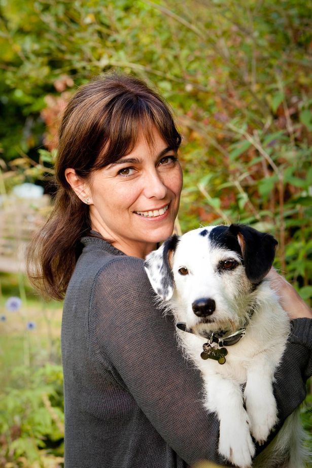 Fiona Dolman smiling and wearing a gray blazer while carrying a dog.