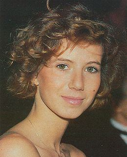 Fiona Gélin with a tight-lipped smile and brown short curly hair while wearing a necklace