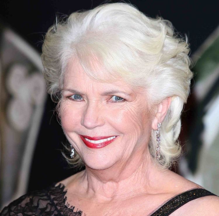 Fionnula Flanagan smiling with red lipstick and wearing a black sleeveless dress.