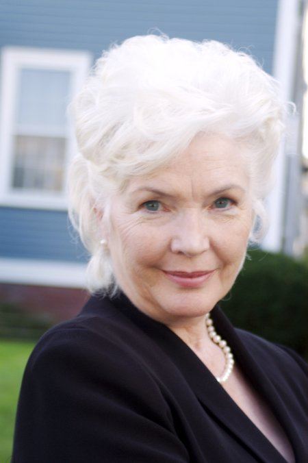 Fionnula Flanagan smiling closed mouth and wearing a black dress and a pearl necklace.