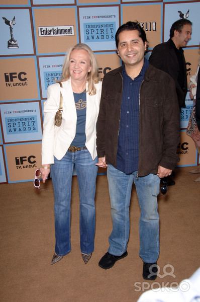 Firdous Bamji smiling with Hayley Mills and wearing a blue long-sleeved shirt under a brown jacket along with jean pants.