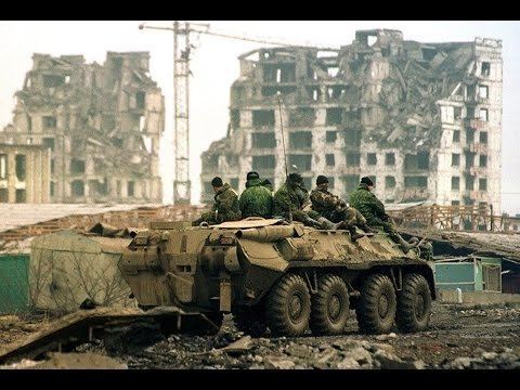 Russian troops riding on the tank during the Chechen War while destroyed buildings can be seen