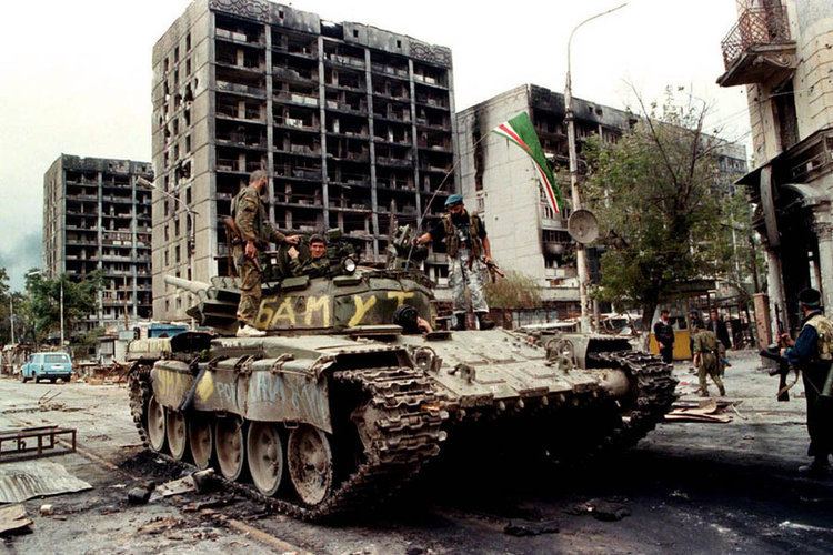A group of a soldier riding on the tank during the Chechen War while destroyed buildings can be seen