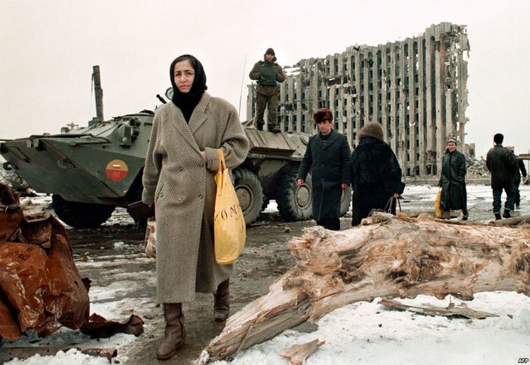 Chechen women and men pass by a Russian armoured personnel carrier in front of the destroyed presidential palace in Grozny