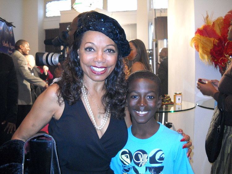 Florence LaRue smiling while wearing black hat and black dress with the boy beside him wearing blue printed shirt