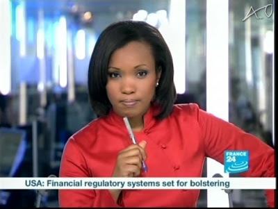 Folly Bah Thibault reporting the news while holding a ballpen and  wearing a red blouse and earrings