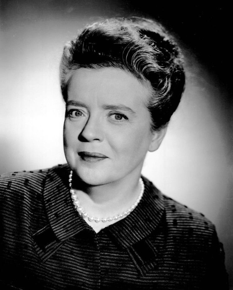 Frances Bavier with a tight-lipped smile and short hair while wearing a pearl necklace and blouse