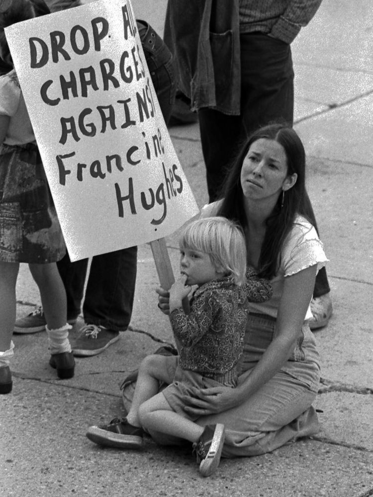 A woman sitting on the ground with a little girl holding a placard saying, "Drop all charges against Francine Hughes".