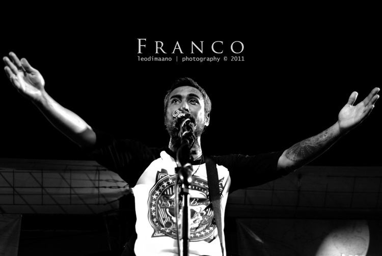 Franco Reyes of Franco band is singing while his arms are wide open in one of their concerts, and he is wearing a t-shirt with a skull design