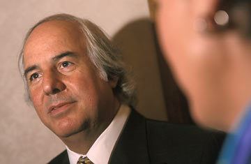 Frank Abagnale looking at something while wearing a black coat over a white suit and a necktie.