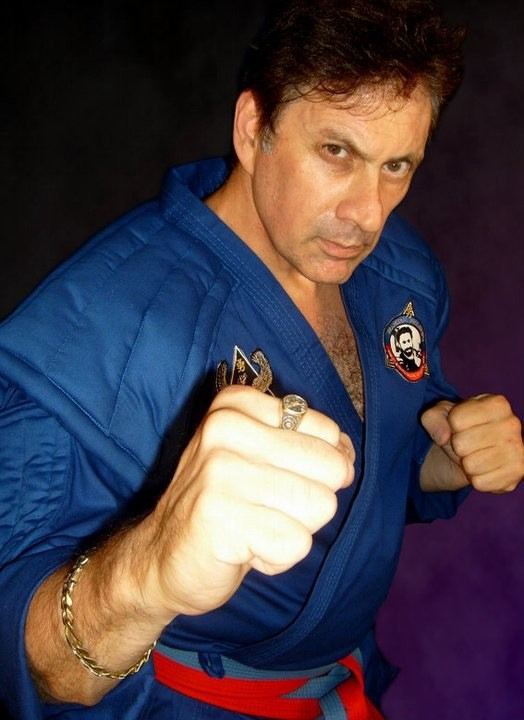 Frank Dux in his martial arts pose while wearing blue dobok and gold bracelet and ring