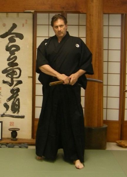 Frank Dux wearing black dobok while holding his weapon