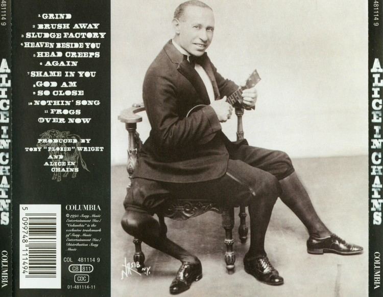 Frank Lentini smiling and sitting on the chair while holding a small guitar on the back cover of the rock band Alice in Chains's 1995 self-titled album. Frank is wearing pants, high socks, shoes, and a long sleeve under a necktie and a coat