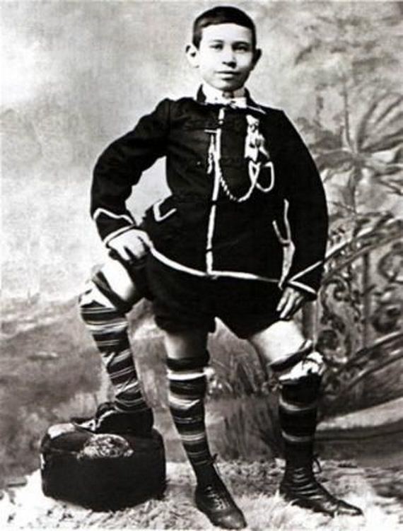 Frank Lentini with a tight-lipped smile while hands on his hips and his left foot is on the rock,  wearing shorts, shoes, striped high socks, and a coat