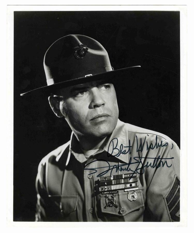 Frank Sutton turning sideways while wearing an officers attire for his role as Gomer Pyle, U.S.M.C. with his own signature at the bottom right.