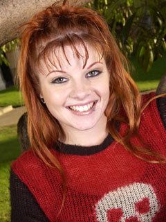 Frankie Abernathy smiling with an orange hair while wearing a black and red blouse