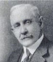 Franklin Clarence Mars with mustache while wearing long sleeves, necktie, and coat