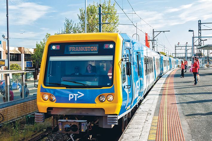 A yellow and blue train on a Frankston railway line with passengers waiting on the right side