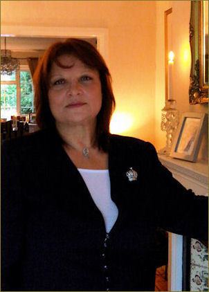 Françoise Pascal is wearing a black blazer, white inner blouse, and necklace